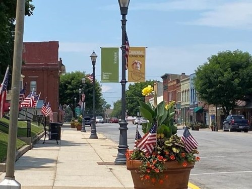 A quiet street lined with shops, decorated with American flags and flower planters under a clear blue sky.