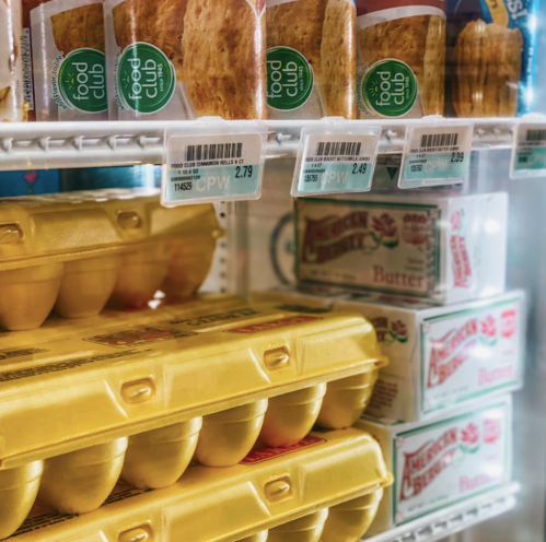 Grocery shelf with food items: eggs, butter, and snacks in packaging, with price tags visible.