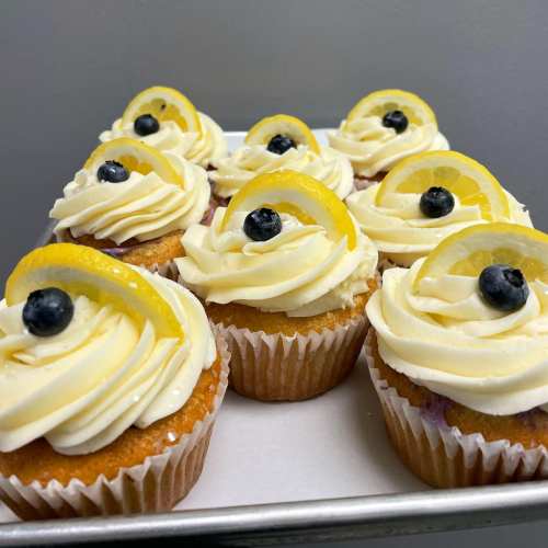 A tray of lemon blueberry cupcakes topped with swirls of frosting, lemon slices, and blueberries.