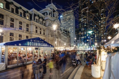 A bustling city scene at night with festive lights, featuring a welcome sign for the Rothman Cabal and people walking by.