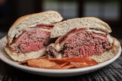 A close-up of a juicy burger with layers of beef, bacon, and cheese, served with crispy potato chips on the side.