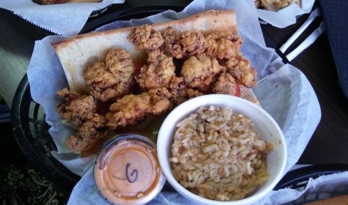A plate featuring fried chicken on bread, a side of rice, and a small container of sauce.