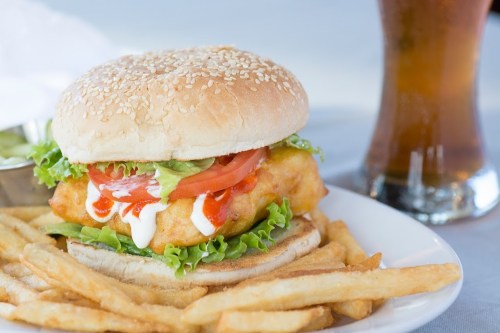 A sesame seed bun burger with lettuce, tomato, and sauce, served with fries and a glass of soda.