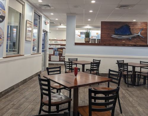 Interior of a restaurant featuring wooden tables, black chairs, and a large fish mural on the wall.