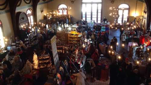 A bustling indoor market filled with vendors and shoppers, decorated with lights and holiday items.
