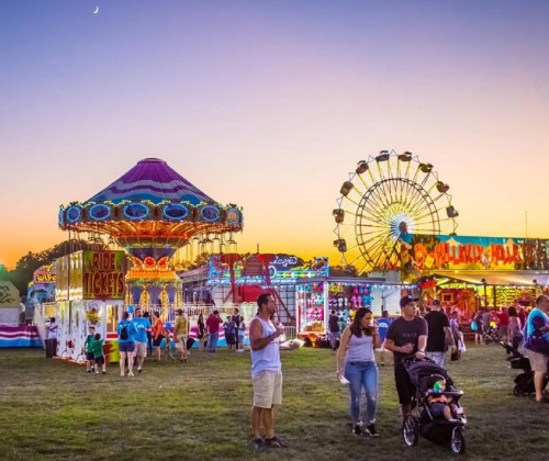 A vibrant carnival scene at dusk, featuring rides, games, and families enjoying the festivities.