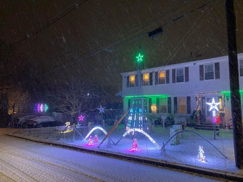 A house decorated with colorful lights in a snowy scene, with falling snow and a festive atmosphere.