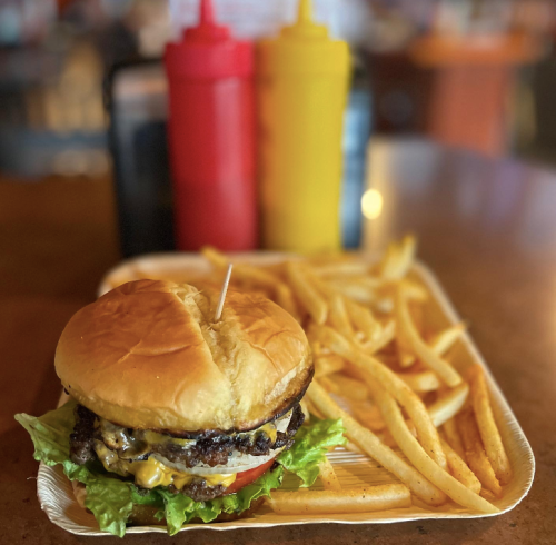 A juicy cheeseburger with lettuce and tomato, served with golden fries and condiments in the background.