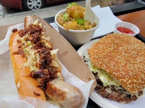 A plate featuring a loaded sausage sandwich, a burger with lettuce, and a side of seasoned potatoes.