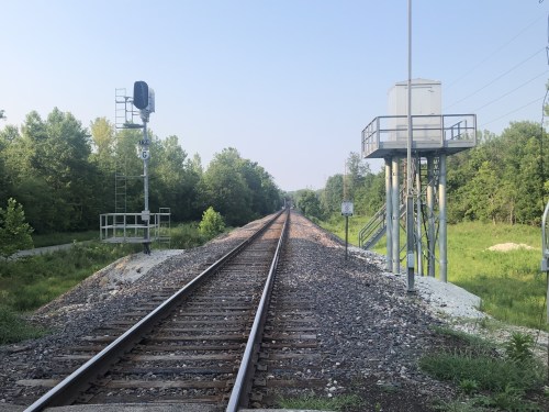 A view of railway tracks stretching into the distance, flanked by trees and signal equipment on either side.