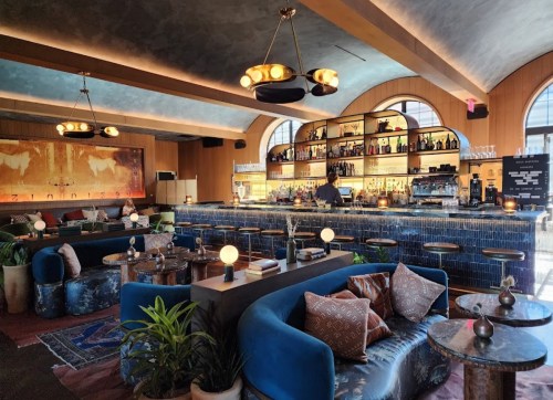 A stylish bar interior featuring blue seating, a well-stocked bar, and warm lighting in a cozy atmosphere.