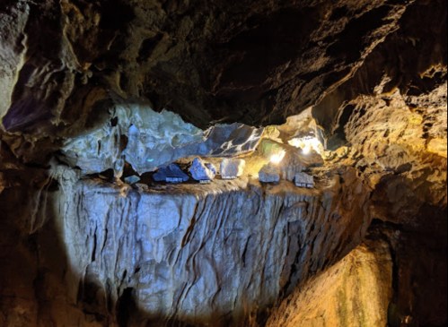 A dimly lit cave interior with rocky formations and small structures illuminated by soft lights.