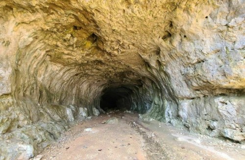 A rocky cave entrance with textured walls and a dark interior, leading into a natural tunnel.