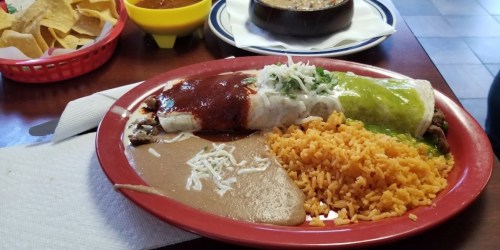 A plate of enchiladas with red and green sauce, rice, refried beans, and garnished with onions and cilantro.