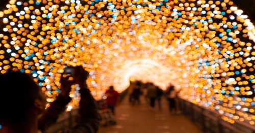 A person takes a photo in a tunnel illuminated by vibrant, colorful lights, creating a magical atmosphere.
