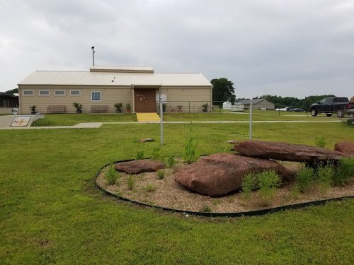 A single-story building with a metal roof, surrounded by grass and large rocks, under a cloudy sky.