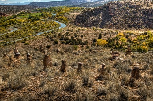 A scenic landscape featuring stacked stones on a hillside, overlooking a winding river and lush greenery below.
