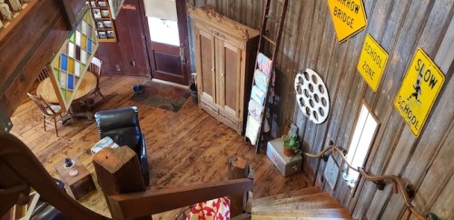 Cozy interior of a rustic cabin with wooden walls, a staircase, and vintage signs, featuring a small dining area.