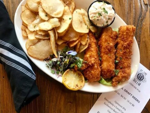 A plate of crispy fried fish fillets with potato chips, a side of coleslaw, and a lemon wedge on a wooden table.