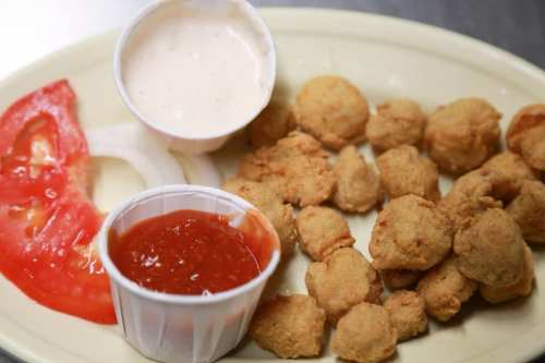 A plate of fried food with dipping sauces, sliced tomato, and onion rings on the side.