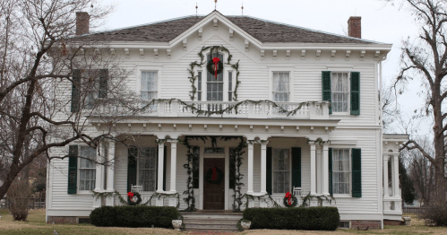 A large white historic house decorated with green garlands and red wreaths for the holiday season.