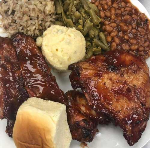 A plate of barbecue ribs, chicken, rice, green beans, baked beans, cornbread, and a dinner roll.