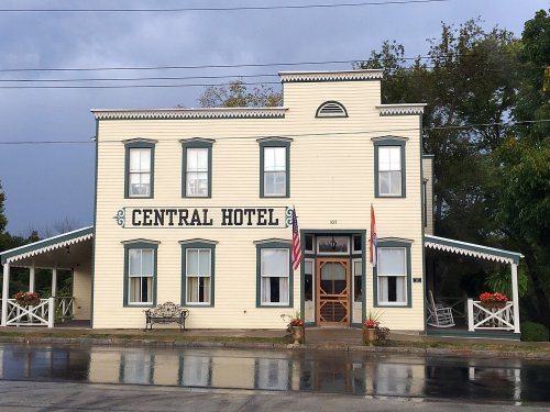 A two-story white building with "Central Hotel" painted on the front, featuring a porch and American flag.