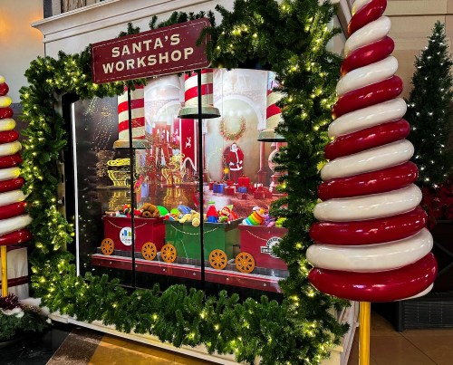 A festive display of Santa's Workshop with colorful toys, a Santa figure, and holiday decorations surrounded by greenery.