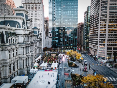 Aerial view of a city ice skating rink surrounded by tall buildings and autumn trees.