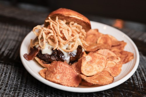 A juicy burger topped with melted cheese and crispy onions, served with a side of golden potato chips.