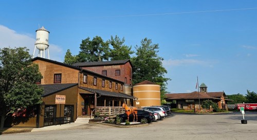 A rustic building with a water tower, surrounded by trees and parked cars, under a clear blue sky.