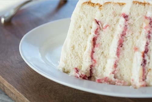 A slice of white cake with layers of cream and raspberry filling on a white plate.