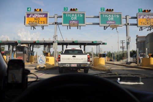 View from inside a car at a toll booth with signs for tickets and EZ-Pass, showing a white truck in line.
