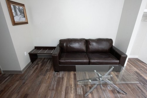 A modern living room featuring a brown leather sofa, a glass coffee table, and wooden flooring.