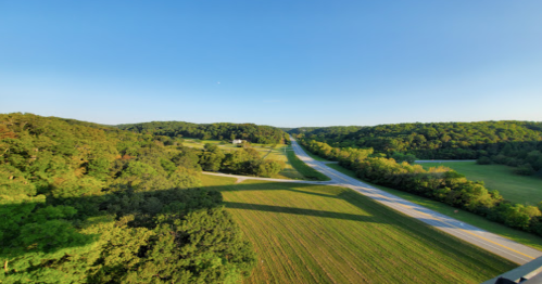 A scenic view of a winding road surrounded by lush green fields and hills under a clear blue sky.