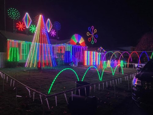 A brightly lit house decorated with colorful Christmas lights, featuring a tree, arches, and festive designs at night.