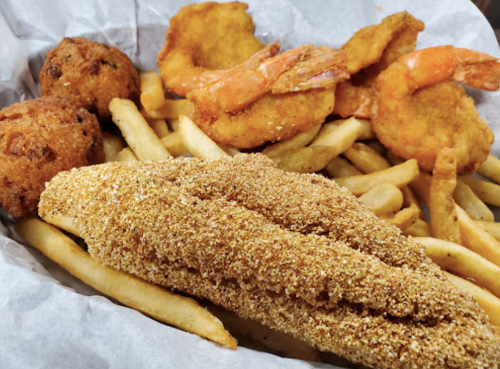 A basket of fried fish, shrimp, hushpuppies, and French fries on parchment paper.