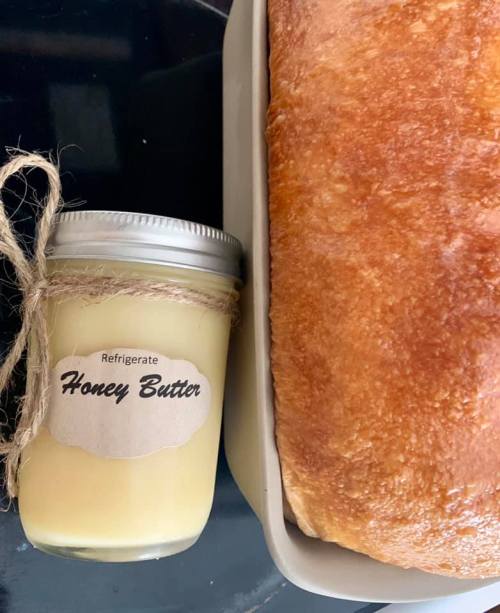 A jar of honey butter with a twine bow next to a freshly baked loaf of bread on a black surface.
