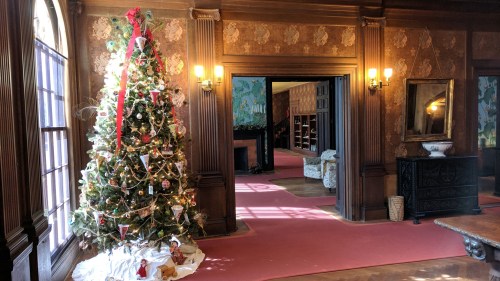 A beautifully decorated Christmas tree stands in a warmly lit room with vintage decor and a pink carpet.