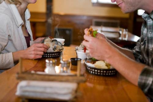 Two people enjoy a meal at a wooden table, with steaming dishes and condiments in a cozy restaurant setting.