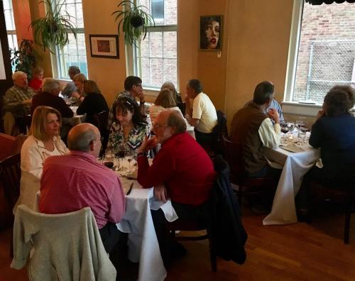 A cozy restaurant scene with diners engaged in conversation around tables, surrounded by warm lighting and decor.