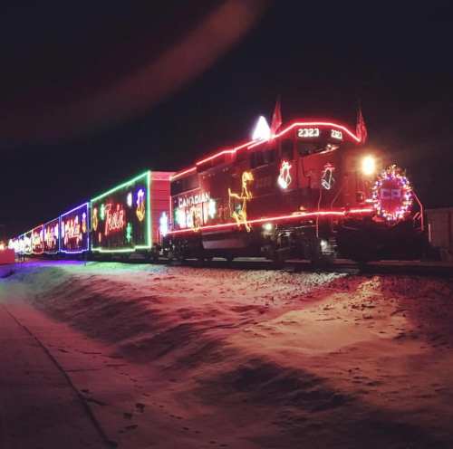 A brightly lit train decorated with colorful holiday lights travels through a snowy landscape at night.