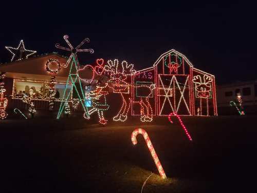 Colorful holiday lights decorate a barn and yard, featuring candy canes, reindeer, and festive decorations at night.