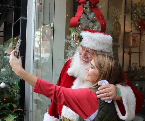 A smiling Santa Claus and a woman take a selfie together in a festive, decorated setting.