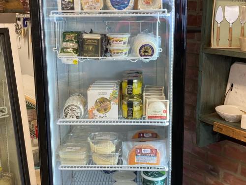 A glass-front refrigerator filled with various cheese products and spreads on shelves.
