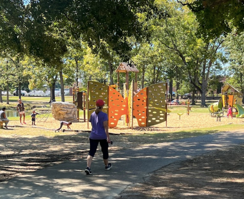 A playground with colorful butterfly structures, children playing, and a person walking on a path nearby.