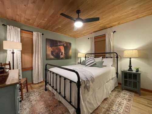Cozy bedroom with a metal bed frame, warm lighting, wooden ceiling, and decorative rugs.