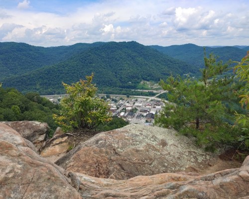 A scenic view from a rocky overlook, showing a small town nestled in a valley surrounded by green mountains.