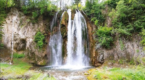 A picturesque waterfall cascading over rocky cliffs, surrounded by lush greenery and trees.