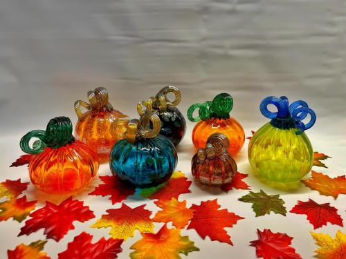 Colorful glass pumpkins in various sizes surrounded by vibrant autumn leaves.